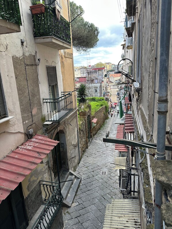 Une ruelle étroite pavée, bordée d’immeubles dotés de balcons, dont certains sont ornés de plantes.