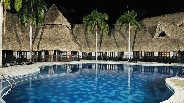 A swimming pool with a geometric tile pattern, surrounded by thatched-roof structures and palm trees. - Relax in Flandes Tolima, apartment with Swimming Pool (Flandes)
