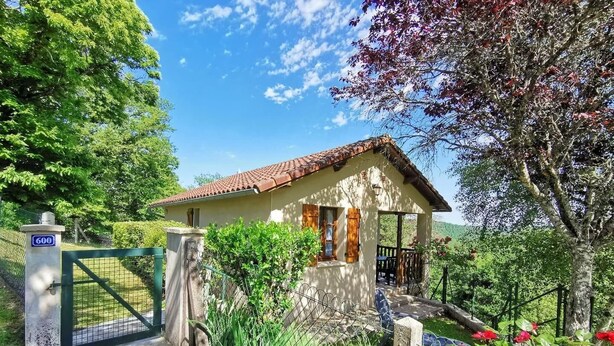 A small, single-story house with a tiled roof, a porch, and a fenced yard with red flowers. - Gîtes de France® - La Belle Vue (SAINT PERDOUX)
