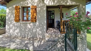 A small, single-story house with a porch, wooden shutters, and a small garden area with pink flowers. - Gîtes de France® - La Belle Vue (SAINT PERDOUX)