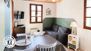 A cozy room with a wooden ceiling, a green sofa, a dining table with chairs, a TV, and a window with a view. - Gîtes de France® - La Belle Vue (SAINT PERDOUX)