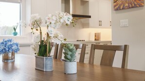 A dining table with two potted plants, a window with a view, and white cabinetry in a kitchen setting. - Bright Lakeside Cottage | 4br & 16 guest max | Private Dock & Nature Retreat (Georgina)