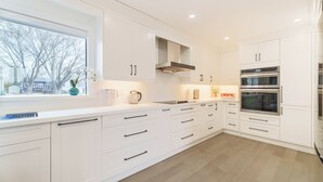 A modern kitchen with white cabinetry, a large window, and built-in appliances. - Bright Lakeside Cottage | 4br & 16 guest max | Private Dock & Nature Retreat (Georgina)