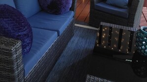 A cozy seating area with a blue sofa and wicker chairs, a decorative mirror, and a string of lights on a striped backdrop.