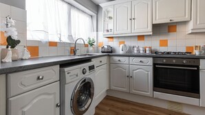 A modern kitchen with white cabinetry, a built-in washing machine, a gas stove, and a coffee maker. - Spacious 3-Bedroom Home in Basildon, Essex London (Basildon)