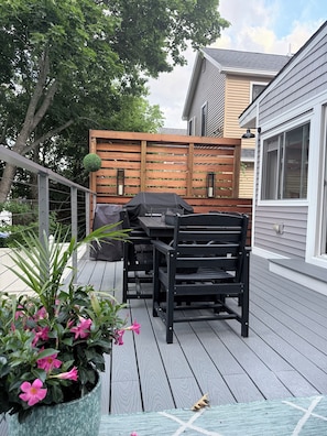 Une terrasse avec un barbecue, des chaises et une clôture en bois.