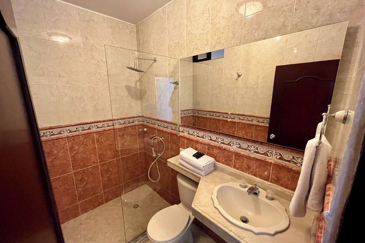 Uma casa de banho moderna com cabine de duche em vidro, sanita branca e lavatório com espelho em cima.