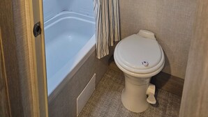 A compact bathroom with a bathtub, toilet, and wooden cabinets.