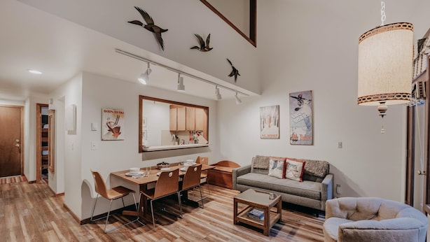 A modern living room with a dining area, wooden flooring, a sofa, a coffee table, and decorative bird wall art. - Condo 91sw With a River View and Close to Community Amenities (Deming)