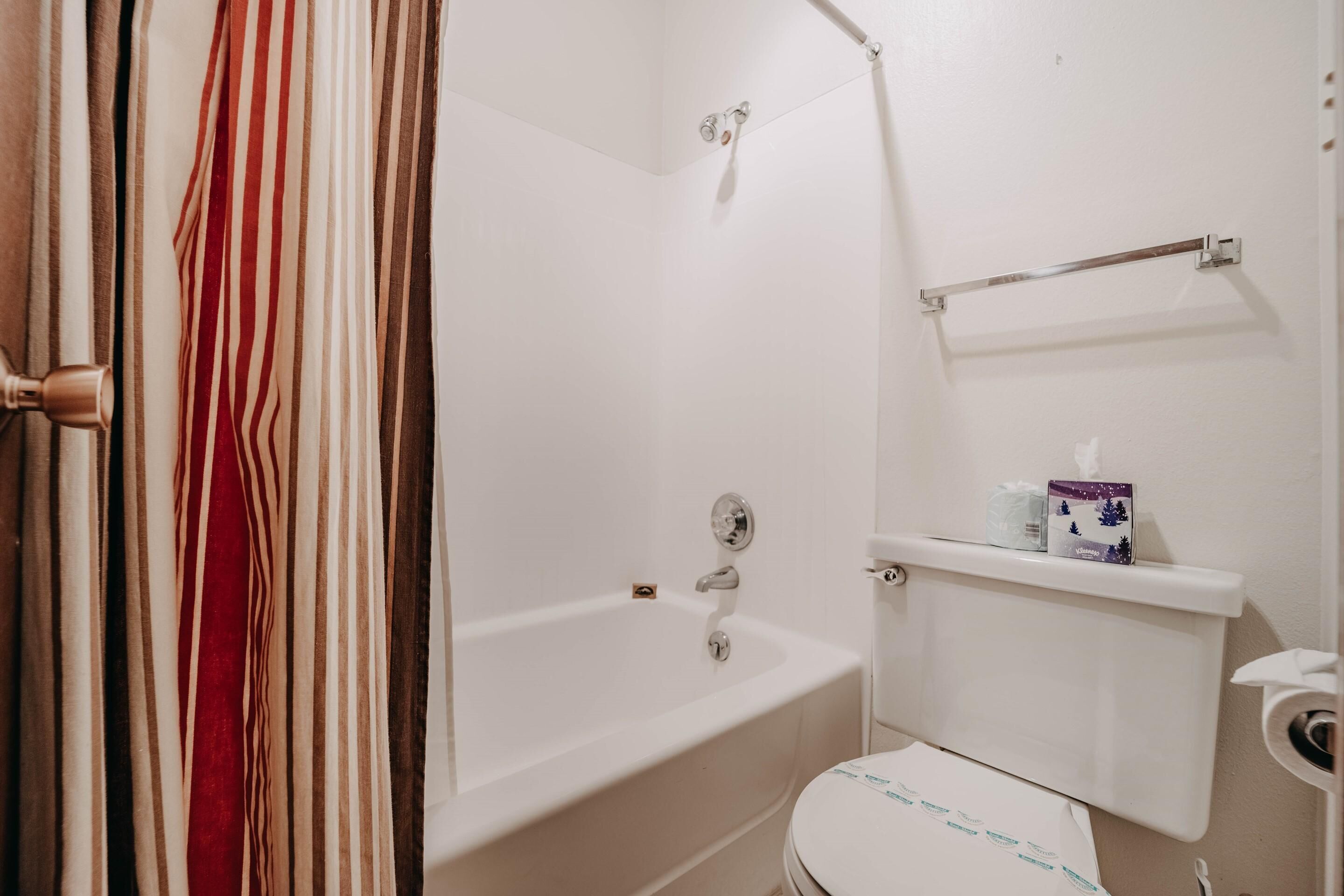 A bathroom with a bathtub, toilet, and a shelf with toiletries.