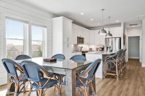 A modern kitchen with white cabinets, a glass island, and wicker chairs. - Stay Happy as a Clam – Your Coastal Escape in Carolina Beach! (Carolina Beach)
