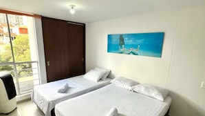 Hotellihuone, jossa on kaksi sänkyä, suuri ikkuna ja taulu seinällä.