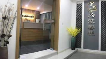 A reception area with a modern design, featuring a reception desk, a wall-mounted sign with Chinese characters, and a vase with yellow flowers.