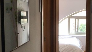 A bedroom with a bed, a large mirror, and a window with a view of greenery. - Weibo Inn (Shanghai Zhongshan Park) (Shanghai)