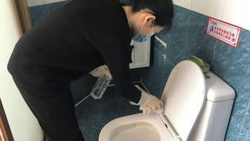 A person cleaning a toilet in a bathroom with blue tiles and a sign on the wall.