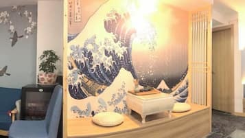 Quarto com pintura tradicional japonesa de ondas, uma mesa de recepção, uma cadeira azul e uma planta.