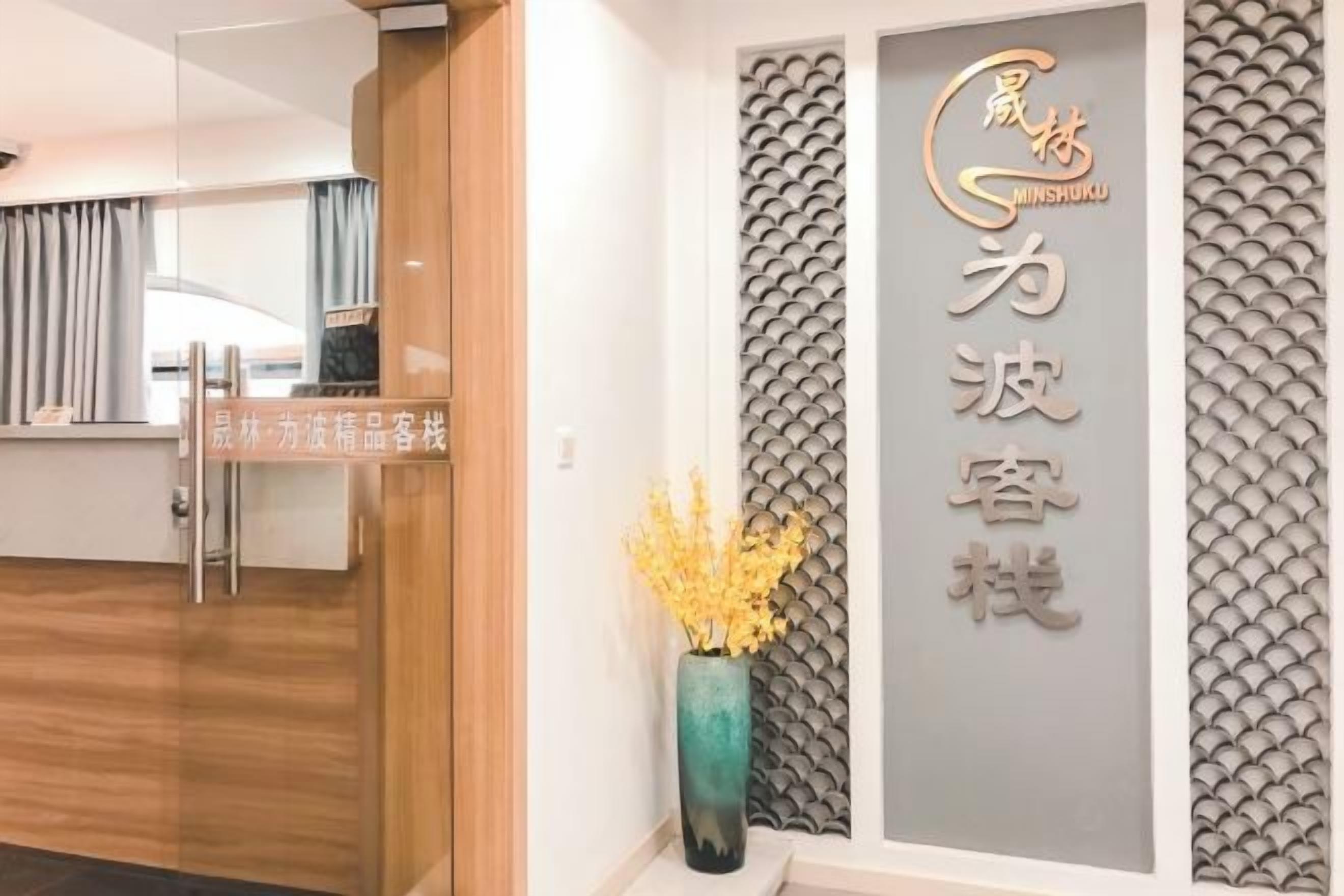 A reception area with a wooden reception desk, a wall-mounted sign with Chinese characters, and a decorative vase with yellow flowers.
