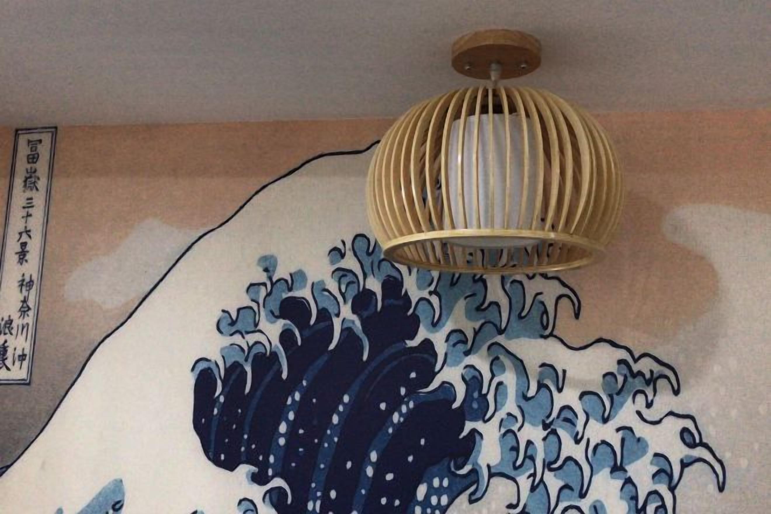 Une pièce dont un mur est orné d’un tableau représentant des vagues, avec un luminaire au plafond et un panneau fixé au mur, portant des caractères japonais.