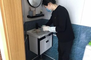 A person in a black uniform cleaning a bathroom sink. - Weibo Inn (Shanghai Zhongshan Park) (Shanghai)