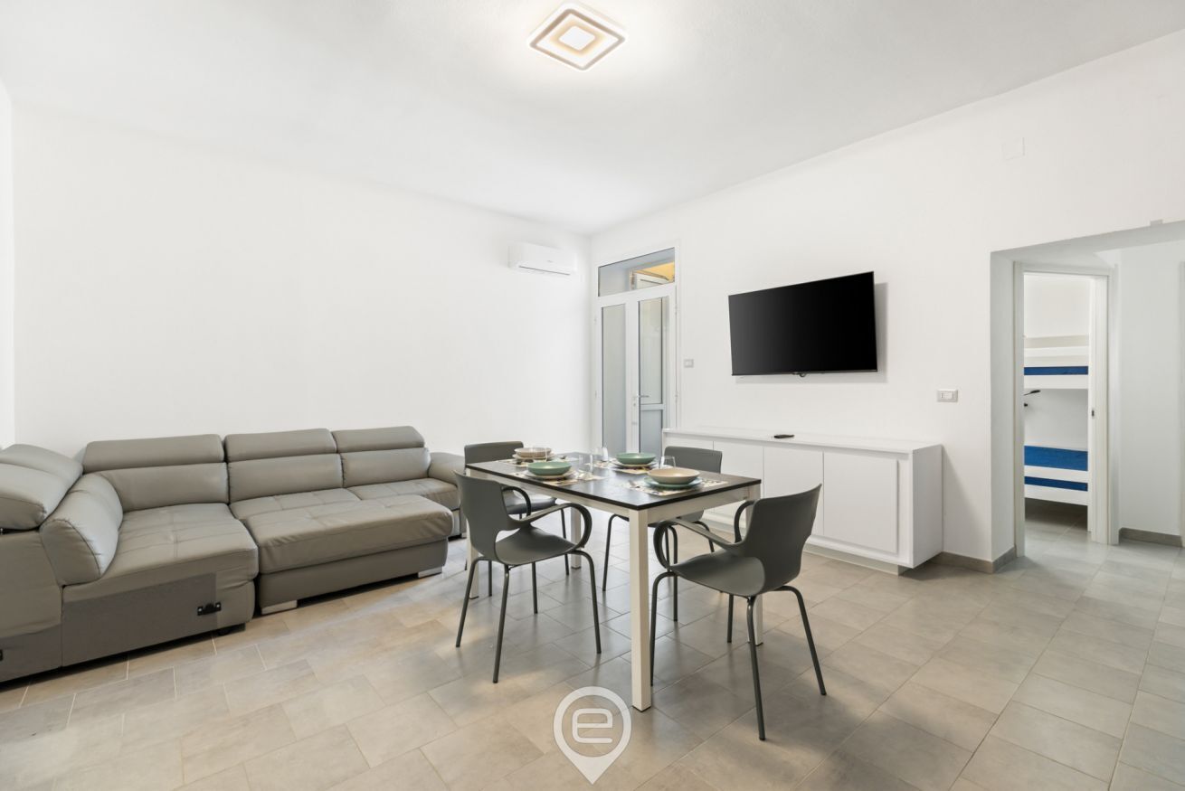 Een moderne woonkamer met een bank, eettafel, stoelen, een flatscreen televisie en een kledingkast.