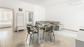 A modern, well-lit living area with a dining table, chairs, a sofa, and a white air conditioning unit. - Alguerìta Apartment - Alghero (Alghero)