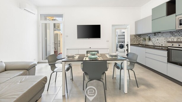 A modern kitchen with a flat-screen TV, a dining table with chairs, and a built-in oven. - Alguerìta Apartment - Alghero (Alghero)