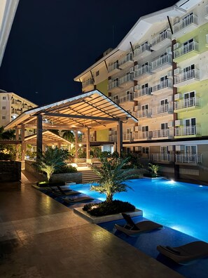Un hotel a più piani con balconi, una zona relax esterna coperta e una piscina.