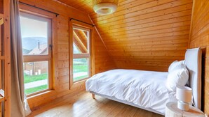 A wooden cabin bedroom with a bed, a window, and a hanging light fixture. - "Domaine la Clairière Le Douglas (Soultzmatt)