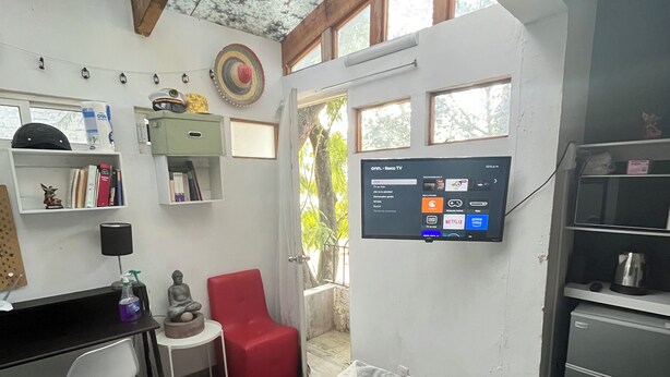 A compact room with a bed, a desk, a red chair, a TV mounted on the wall, and a small kitchenette. - Estudio en Coyoacán - El Balcón de Buda (Mexico City)