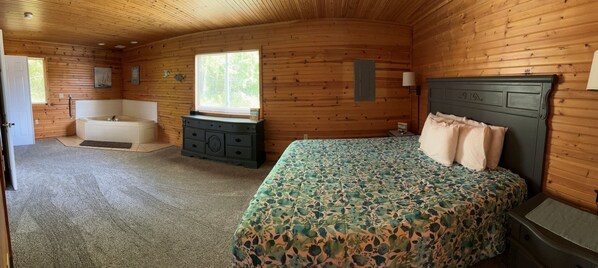 A wooden cabin bedroom with a bed, a dresser, a vanity, and a window. - Scenic Stay | Indoor Pool, Rowboats & Relaxing Nature Views (Gladwin)