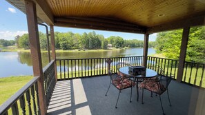 A covered outdoor area with a table and chairs, a view of a lake, and a sign indicating no sitting or standing on the railing. - Scenic Stay | Indoor Pool, Rowboats & Relaxing Nature Views (Gladwin)