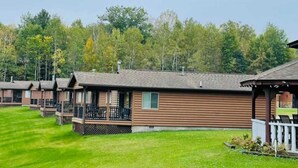 Une rangée de chalets en rondins, dotés de vérandas, entourés d’une pelouse bien entretenue et d’une forêt dense.