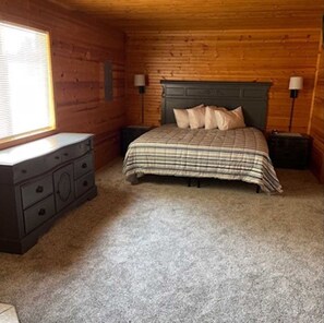 A bedroom with a wooden ceiling, a bed with a plaid bedspread, two bedside tables, a dresser, and a window with blinds. - Scenic Stay | Indoor Pool, Rowboats & Relaxing Nature Views (Gladwin)