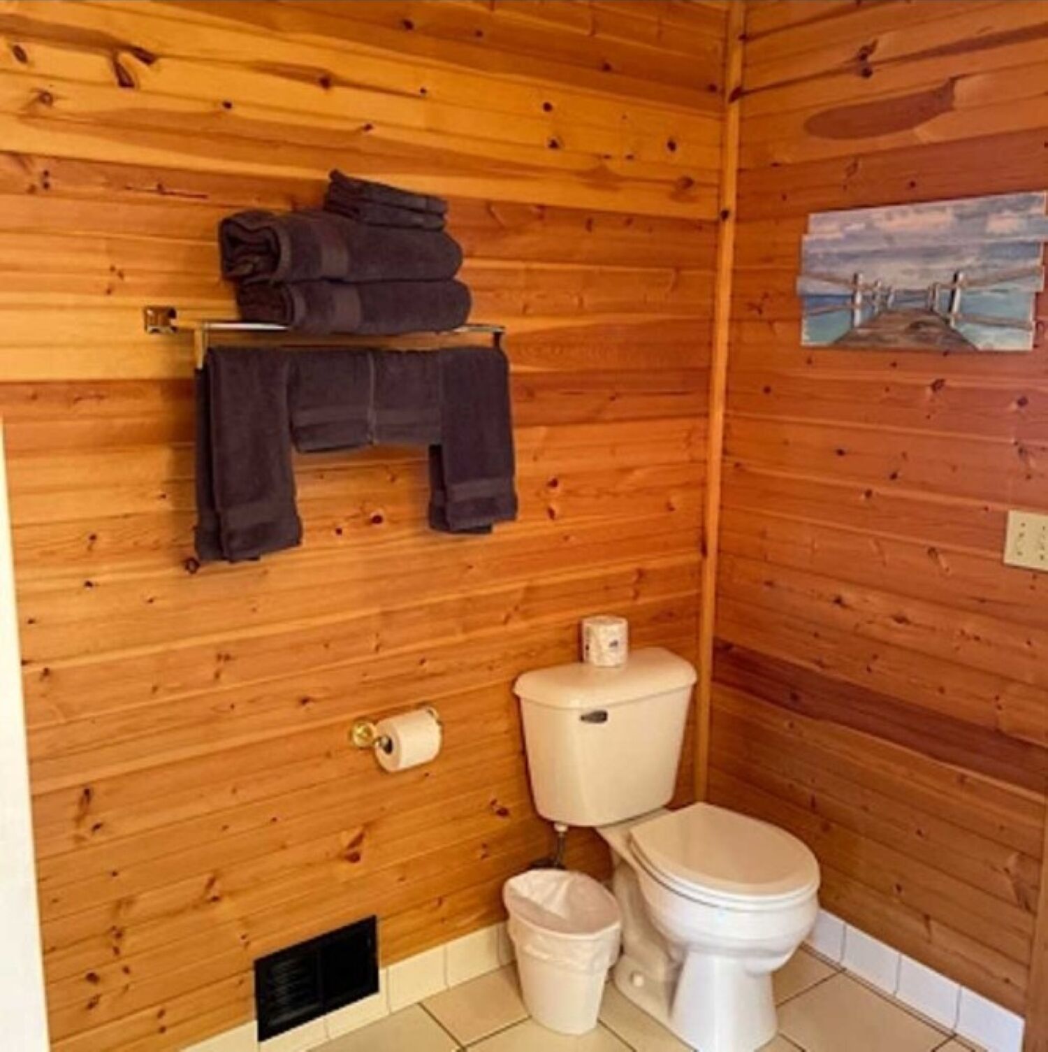 Ein kleines Badezimmer in einer Holzhütte mit Toilette, Waschbecken und einem Regal mit Handtüchern.