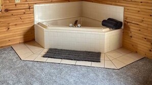 Ein Badezimmer im Eckbereich mit Badewanne, Holzwänden, einem kleinen Teppich und einem Schiffsbild.