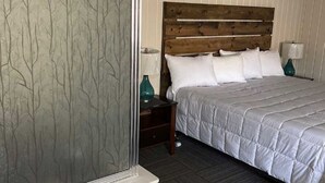Un dormitorio con cabecera de madera, ropa de cama blanca, una mesita de noche con lámpara y ventana con motivo de árbol.