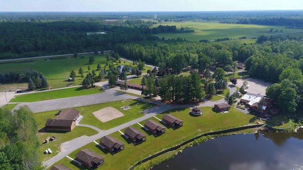 Luchtbeeld van een camping met verschillende blokhutten, een centraal gebouw en een meer.