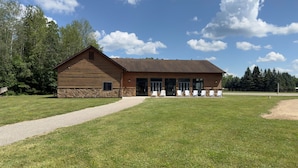 A log cabin with a stone foundation, a gravel path leading to the entrance, and outdoor seating with chairs. - Riverside Romance: Couple Getaway with Cozy Tavern Dining & Indoor Pool Access (Gladwin)
