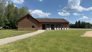 A log cabin with a stone foundation, a gravel path leading to the entrance, and outdoor seating with chairs. - Secluded Cabin Sanctuary with Direct River Access & Indoor Pool (Gladwin)