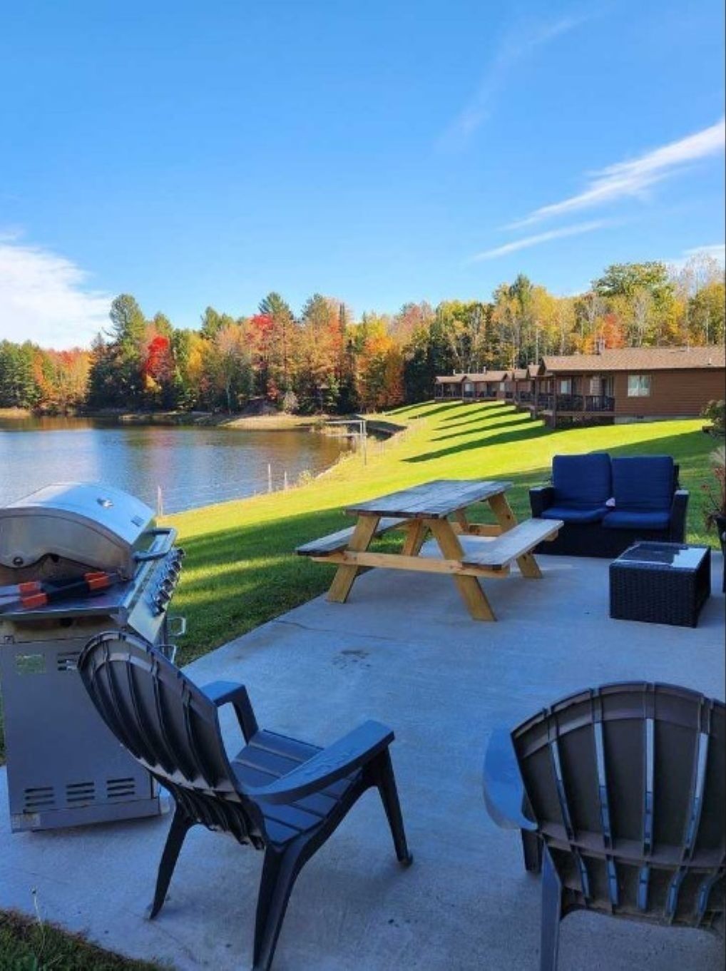 A lakeside patio with a grill, picnic table, and outdoor seating.