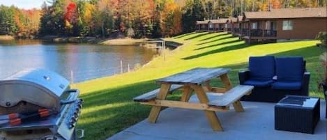 A lakeside patio with a grill, picnic table, and outdoor seating.