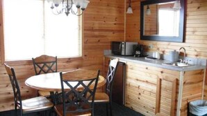 Interno di una baita di legno con tavolo, sedie, angolo cottura, forno a microonde, lavello e pensili.