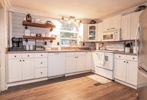 Une cuisine avec des meubles blancs, un four à micro-ondes, une cuisinière et une machine à café.