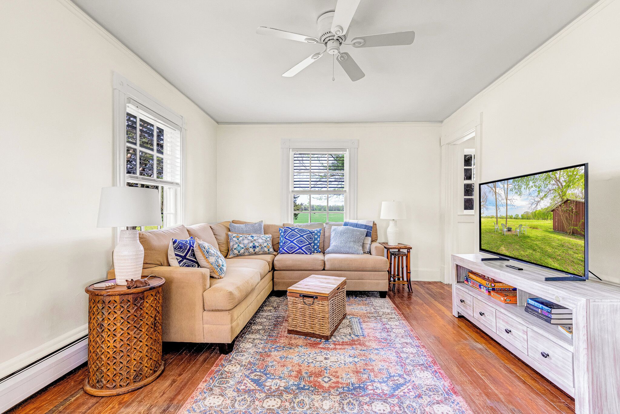 A living room with a sectional sofa, a television, a patterned rug, and a ceiling fan.