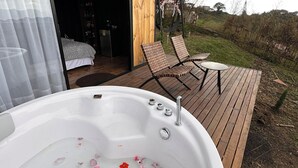 A wooden deck with a hot tub filled with water and flower petals, a swing chair, and a bedroom with a bed and a wardrobe. - Beautiful cabin/glamping in the city of Pereira, with beautiful view. (Pereira)