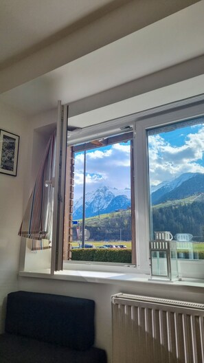 A room with a large window offering a mountain view, a radiator, and a dark-colored sofa. - Residence Alpin TOP 3 - Kaprun Incl Summer Card (Kaprun)