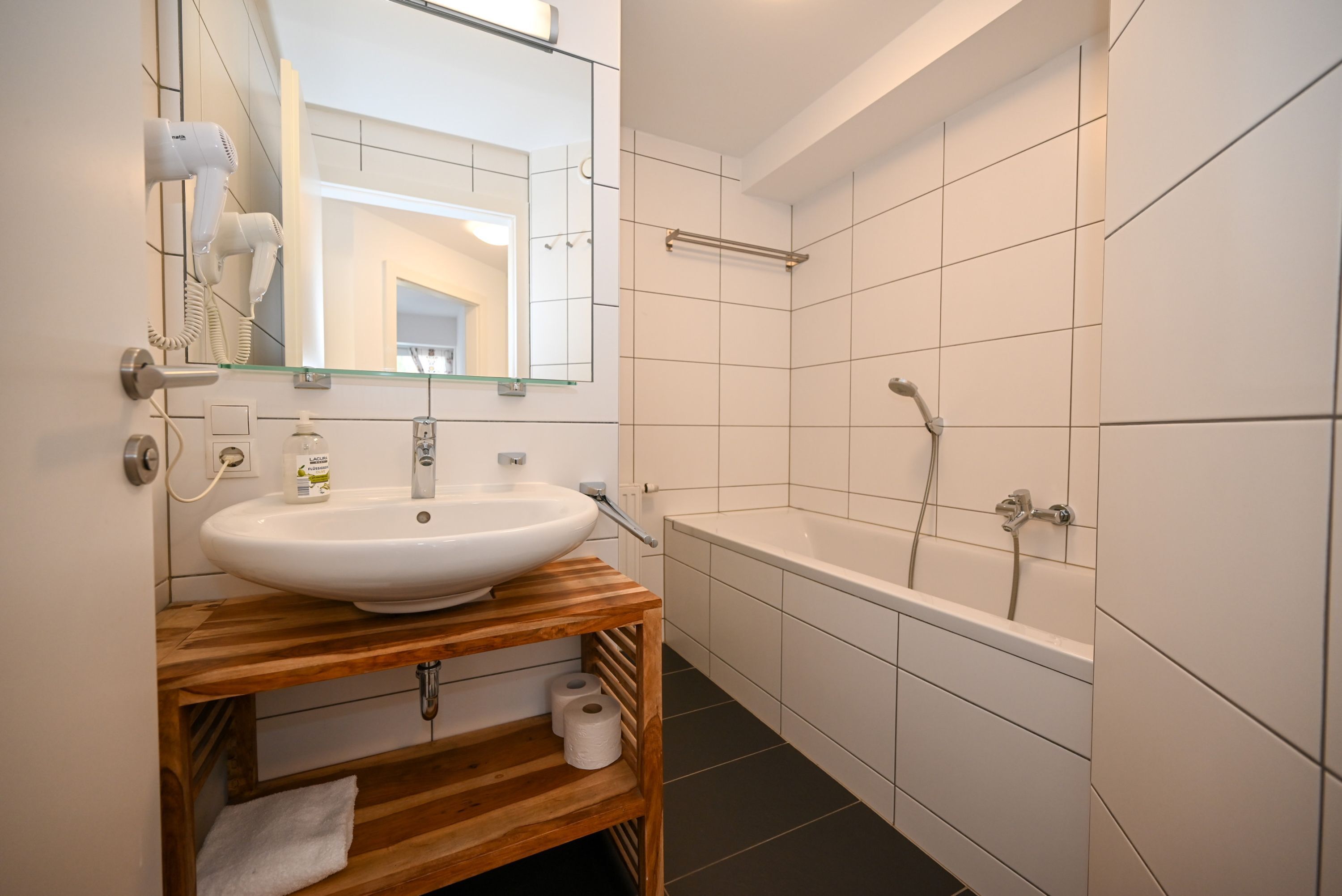 Une salle de bain moderne avec un meuble-lavabo en bois, un lavabo blanc et un grand miroir.