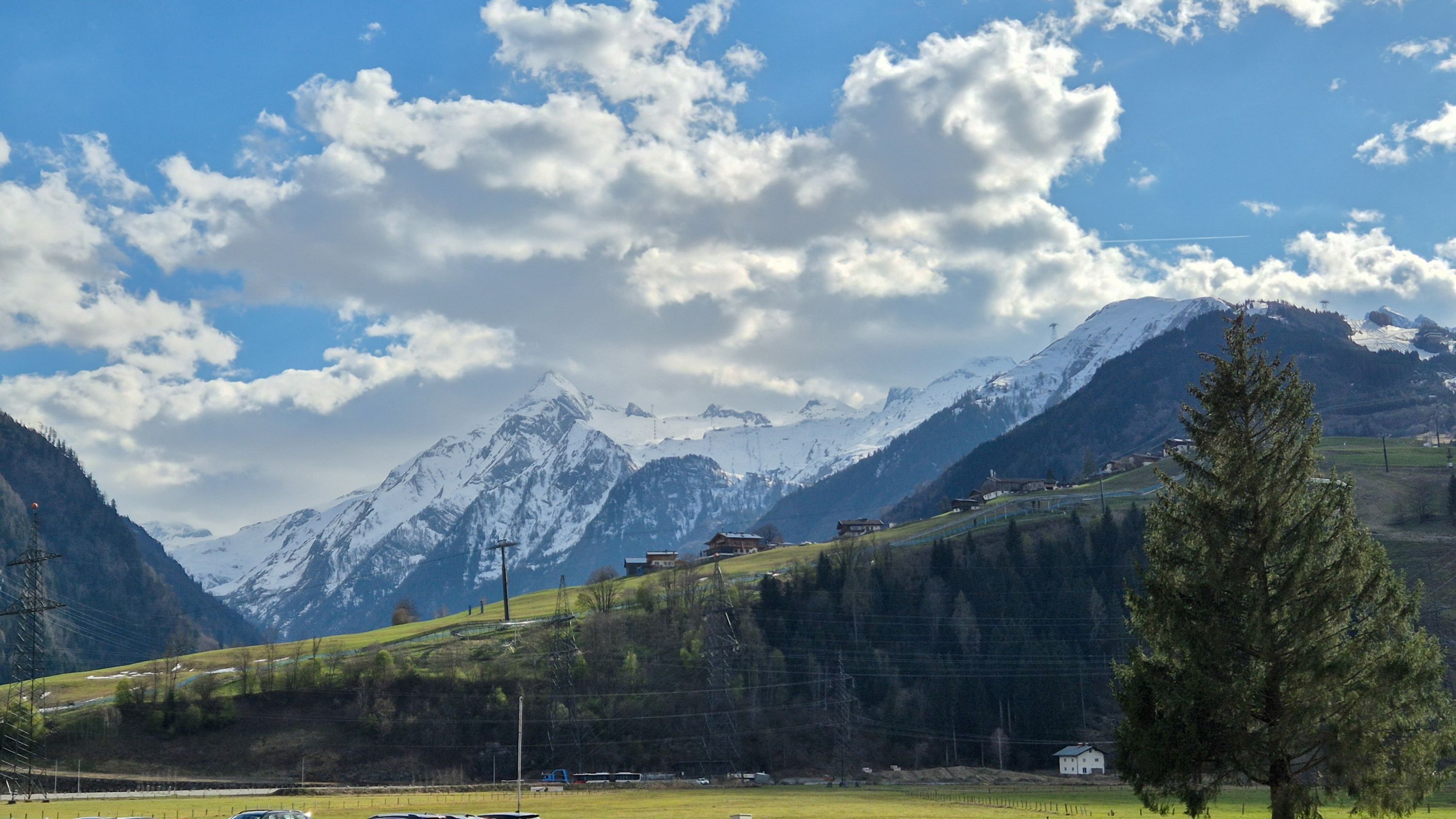 A mountainous landscape with snow-capped peaks, a clear sky, and a few buildings on a hillside.