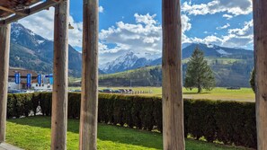 A view from a wooden structure overlooking a parking area, a green field, and a mountain range with snow-capped peaks. - Residence Alpin TOP 3 - Kaprun Incl Summer Card (Kaprun)