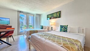 A hotel room with two beds, a desk with a TV, and a view of the city. - Luana Waikiki Hotel & Suites 119-Modern Waikiki Studio,2 Beds,AC,WiFi,Pool & Gym (Honolulu)
